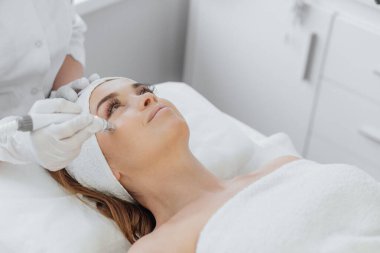 Radiofrequency facial skin lifting. Hardware cosmetology RF lifting procedure and hardware facial massage. Rejuvenation, skin care in a beauty salon. Woman doctor cosmetologist and girl in spa clinic.