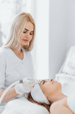 Radiofrequency facial skin lifting. Hardware cosmetology RF lifting procedure and hardware facial massage. Rejuvenation, skin care in a beauty salon. Woman doctor cosmetologist and girl in spa clinic.