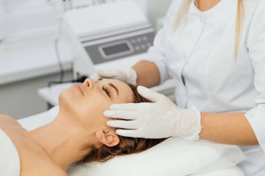 Kadın güzellik uzmanı yüzüne krem sürer. Bakım, rahatlama, gençleşme, yüz bakımı ve kozmetoloji kliniğinde pürüzsüz kırışıklıklar. Güzellik salonunda spa yapan bir kız.