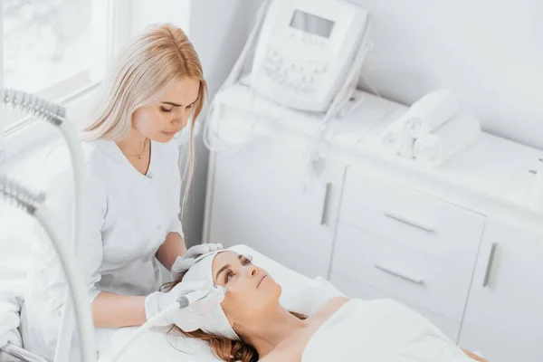 Radiofrequency facial skin lifting. Hardware cosmetology RF lifting procedure and hardware facial massage. Rejuvenation, skin care in a beauty salon. Woman doctor cosmetologist and girl in spa clinic.