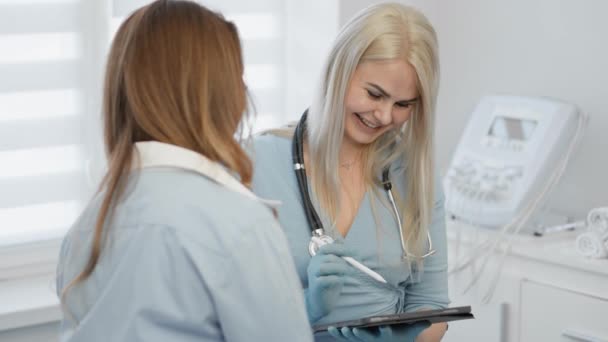 病院の女性患者を診察するタブレット付きの医師 女性医療従事者は診療所の受付で検査を通信し 処方薬を処方する 議論の健康 近代的な治療 — ストック動画