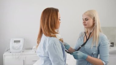 Kadın bir doktor steteskoplu bir hastayı dinler. Muayene olan genç bir kadın. Bir sağlık kliniğinde teşhis konuldu. Hastaneye kabul, kalp ve akciğer hastalıklarının tedavisi