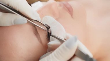 Usta kirpik üreticisi her siliyi doğal kirpiklere düzgünce uyguluyor, hacim ve uzunluk veriyor. Bir kadın, profesyonel bir kozmetikçiyle güzellik kliniğinde kirpik yapıyor. Bakım kombinasyonu