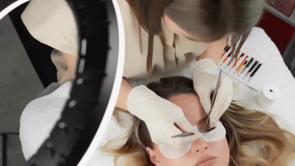 睫毛延伸的过程是在一个现代化的 时尚的化妆品室内使用专业设备进行的 美容院美容师接待处的漂亮姑娘 — 图库视频影像