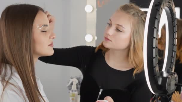 美容師 眉マスターは 特別なツールや技術を使用して表現眉を作成するプロセスを示しています 女性は顔の治療中に美容クリニックでのレセプションでリラックスします — ストック動画
