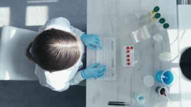 Bir tıp, biyoloji ve kimya araştırmacısı tarafından veri girişi ve araştırma sonuçlarının analizini gösteren bir video klibinin odak noktasındaki klavye ve bilgisayar ekranı. Kameranın üst görüntüsü. Yüksek
