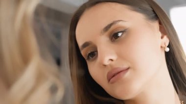 Güzel bir bayan makyöz bir müşteriyle yakın çekim yapar. Güzellik salonu, bir kadını daha çekici ve kendinden emin yapan kişiselleştirilmiş makyaj prosedürleri gerçekleştirir. Yüksek kalite 4k görüntü