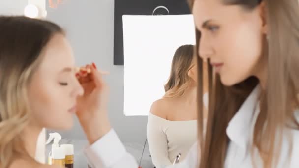 视频片段展示了一位专业人员的工作 他神奇地改变了一个女人的脸 用化妆品在镜子前的美容院里用照明设备创造了一个不可思议的形象 — 图库视频影像