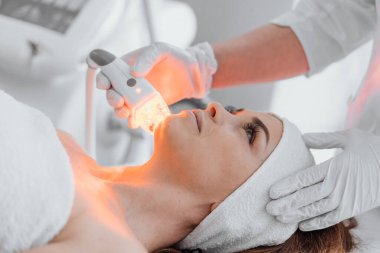 Güzellik uzmanı, hastaların yüz hücrelerini gençleştirmek ve yenilemek için hafif terapi uygular. Genç bir kadın güzellik kliniğindeki bir kozmetikçide resepsiyonda dinleniyor. Yüksek kalite fotoğraf