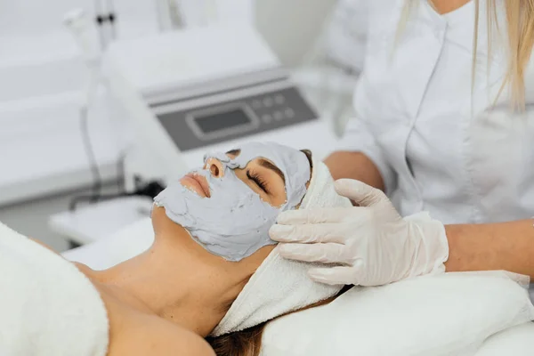A womans face covered with a cosmetic mask is the perfect way to keep your skin in shape and maintain beauty for many years. Beautician in the beauty salon applies a cosmetic mask. High quality photo