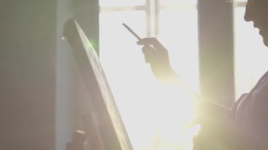 İnce zevkli sanatsal yetenek: fotoğrafta, stüdyodaki genç bir sanatçı günbatımında bir selüette sehpada güzel eserler çiziyor. Boş zaman ve eğlence olarak yaratıcı bir hobi. Sanat terapisi. Yüksek