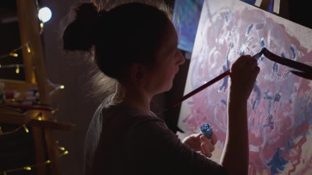 若いアーティストはアートの世界に没頭しており 彼女のスタジオのイーゼルにエレガントなドローイングを描いています 優雅な筆の動きは 才能のある芸術家の創造性を明らかにします — ストック動画