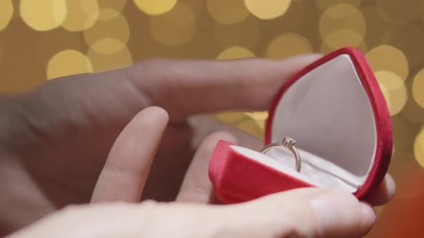 男はギフトの金のダイヤモンドリングを調べ 赤い箱を閉じます 男は彼女のための贈り物 誕生日の宝石を準備しています 背景は集光光型 高品質4K — ストック動画