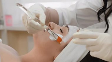 Kaplıca cennetine dalmak: genç bir kadın yüzüne kozmetik bir maske takılarak rahatlar. Cildin güzelliğini ve sağlığını koruyan bir video. Güzel bir prosedür: Güzellik uzmanı...