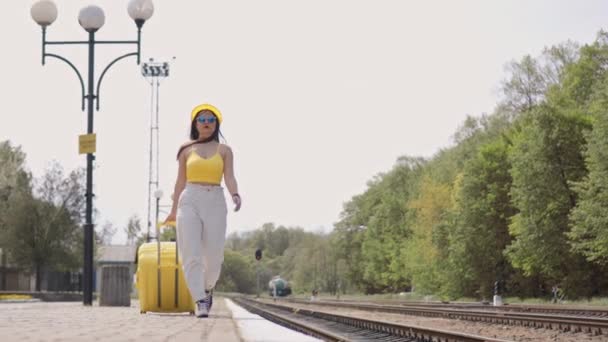 一个戴着太阳镜和行李的年轻女子走在火车站的站台上 期待着人生中美妙的旅游之旅 这个女孩背着一个手提箱要去度假和休息 — 图库视频影像