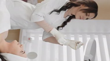 Bir kadının botulinyum tedavisinden zevk aldığı, yüzünü tazelik ve tazeleme ile dolduran bir kozmetolojistin gençlik sihrinin video parçası. Güzellik salonunda dikey video