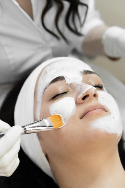 Rahatlama maskesi: bir kadının yüzüne kozmetik maske takmanın bir güzellik kliniğinde cilt bakımı sırasında nasıl rahatlama ve rahatlama hissi yaratabildiği. Yüksek kalite
