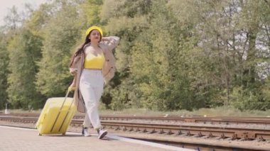 Sarı bir bavul ve yüzünde bir gülümsemeyle, tren peronundaki genç bir kadın bir sonraki büyülü yolculuğundan önce neşesini ifade ediyor. Geçmişe ait anılar ve gelecek yolculuklarının rüyaları.