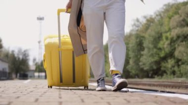 Demiryolu platformunda elinde bavuluyla genç bir kadın, yeni topraklar keşfetmek ve deneyimleriyle kendini zenginleştirmek isteyen modern bir turist imajı çiziyor. Kız spor ayakkabılarla gidiyor ve...