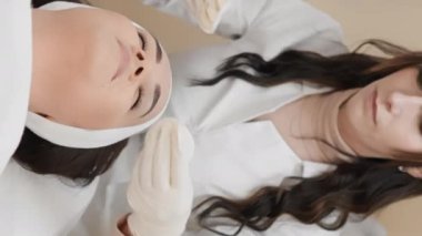 Doğal güzelliğin ifşası: güzellik kliniğinde, kozmetik uzmanı yüzü temizlemeye odaklanır, bir kadının doğal güzelliğini ortaya çıkarır ve cildinin durumunu düzeltir. Dikey video içeri
