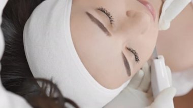 Sağlıklı ve genç yüz: profesyonel bir kozmetikçi tarafından yapılan ultrasonik yüz temizleme, genç görünümlü cildin korunmasına yardımcı olur, yaşlanmanın belirtilerini azaltır. Güzellik kliniğinde dikey video. Yüksek