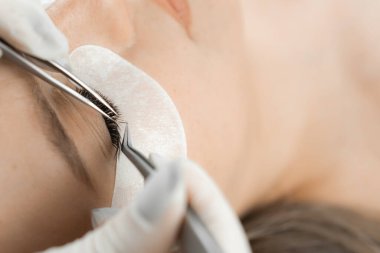 Fotoğraf, müşterinin rahatça uzandığını gösteriyor. Güzellik uzmanı, kirpik uzantıları üzerinde dikkatle çalışıyor. Güzel görünümünü yaratıyor ve güzellik salonunda doğal güzelliğini vurguluyor.