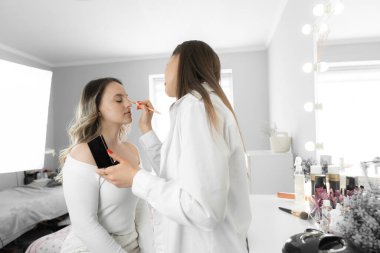 Gelinin sabahı. Genç bir kadın stüdyoda bir makyözle düğün makyajı yapıyor. Güzellik salonunda bir düğün için profesyonel hazırlık. Yandan çekilen fotoğrafın genel planı. Bir