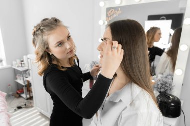 Güzellik salonunda kaş düzeltme işlemi. Usta her fırçayı büyük bir dikkatle uyguluyor. Kadınlara özel bir cazibe veren bir tasarım yaratıyor.