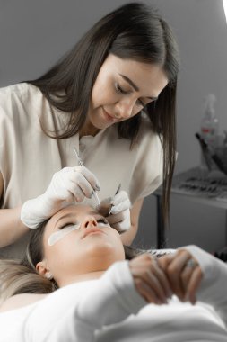 Bir kadın güzellik salonundaki bir güzellik uzmanının ameliyatında rahatlar, ve kirpiklerini dikkatlice uzatır, yüzüne harika bir süsleme efekti yaratır ve güzelliğini vurgular.