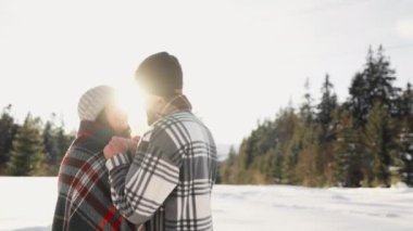 Aşk, mutluluk ve tatil, kışın yürüyen bir çiftin bu videosunu çekiyor. Sevgi dolu erkek ve kız gün batımında karda romantik bir şekilde dururlar. Adam kadının üstünü örttü.