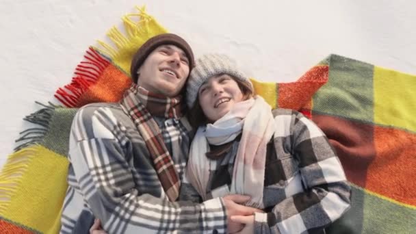 若いカップルが雪の中の毛布の上に横たわり 空を夢見ています 幸せな男と女の町を離れて滞在し 一人でリラックスした 自然の中で冬のリラクゼーション 雪の中に横たわる — ストック動画