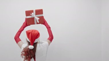Kırmızı elbiseli bir kadın şık bir hediyeye sahip, yeni yıl şenliklerinde beklentiler ve öngörülemez anlar yaratıyor. Beyaz arka planda Noel Baba şapkalı kız geri döndü. Yüksek