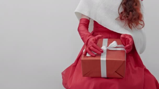 赤いドレスを着たお祝いのチューニングされた赤毛の女性は 喜んでクリスマスと新年の楽しい瞬間を待ってギフトボックスを保持しています 女の子と冬の休日のための贈り物を準備する 高品質4Kについて — ストック動画