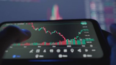 The investor carefully studies the charts and charts of the financial market on his smartphone, analyzing stock movements and market trends. Exchange rate and cryptocurrency prices. High quality 4k