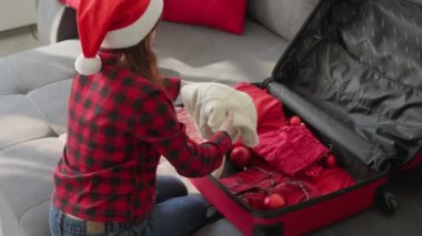Kırmızı Noel Baba şapkalı bir kadın kış tatili için bavulunu hazırlıyor. Kız, tropik bir ülkeye gitmek için kırmızı bavulunu eşyalarla birlikte katlıyor. Yılbaşı ve Noel tatili için tatil