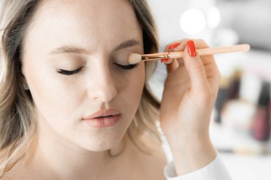 Makyaj sanatçısı göz kapaklarına farklı gölgeler sürdüğünde genç bir kadın gözlerini kapar. Derinlik ve görünüşünü vurgulamak için büyülü bir etki yaratır. Güzellik salonunda makyaj malzemesi.