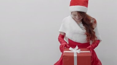 Bir kadın, hediyesini beyaz bir arka planda açmadan önce heyecanla bir anlık heyecan ve beklenti yaratarak hediye kutusunu tutar. Yeni yıl atmosferi ve Noel havası. Yüksek kalite