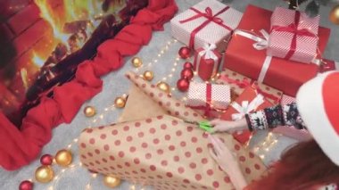 Noel ağacının ışığında, bir kadın hediyelerini dikkatlice sihirli kağıda sarıp her kutuya bir sıcaklık ve kutlama hissi ekler. Kadınların elleri, hediyeleri kaliteli bir kağıda sarar.