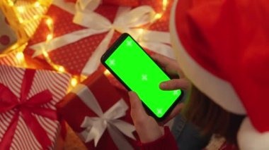 Bir Noel ağacının ışığı altında, elinde akıllı telefon olan bir kişi online alışveriş yapar, hisse senetlerini kontrol eder ve internet üzerinden konaklama olanağı sağlar. Krom anahtarın etkisi. Yeşil Ekran