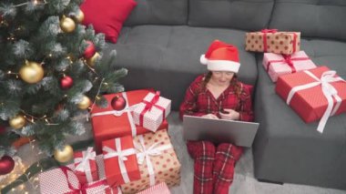 Hediyelerle dolu bir Noel ağacının büyülü atmosferinde, bir kadın bir dizüstü bilgisayarda çalışmaya, alışverişe ve sevdikleriyle çevrimiçi iletişim kurmaya derinden dalmıştır.