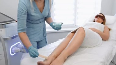 Seçkin bir güzellik salonunda, bir kadın fotoepilasyondan zevk alır, yüksek seviyede uzman yeteneklerine güvenir. Güzellik uzmanı saç çıkarma işleminden önce koruyucu krem sürüyor. Yüksek kalite 4k görüntü