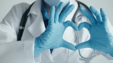Sağlığa tıbbi bakım: steteskop ve eldivenli bir doktor, kalp senfonisini parmakları ve avuçlarıyla gösteriyor, kaliteli tıbbi bakım sağlamaya hazır. Sağlık için aşk