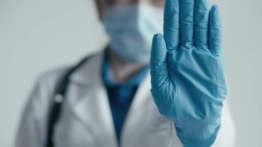 Bir kadın tıp çalışanı elini bu konseptte bir jest olarak gösterir: dur, dur, yasak, giriş imkansızdır, dur. Doktor izin vermez ve durur. Beyaz önlüklü, mavi koruyucu eldivenli ve...