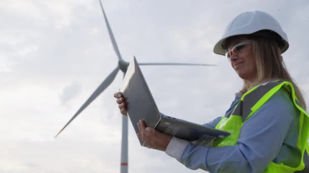 在风车附近配备笔记本电脑的工程师 分析风力涡轮机用于绿色能源的功率 涡轮机科学家 一个由笔记本电脑驱动的风力发电场项目是可持续能源的未来 — 图库视频影像