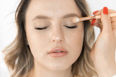 Bu fotoğrafta, bir güzellik salonunda makyaj yapan genç bir kadının çekici yüzü gösteriliyor. Makyaj sanatçısı doğal güzelliğini başarıyla vurgular ve güzelliğin eşsiz bir görüntüsünü yaratır.