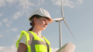 Kadın mühendis, verileri karşılaştırarak evlere sürdürülebilir yeşil yenilenebilir enerji sağlamak için rüzgar türbininin sorunsuz çalışmasını sağlıyor. Koruyucu kasklı ve işaret jöleli bir işçi.