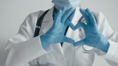 Sağlık koruması: koruyucu maskeli ve eldivenli bir kadın doktor, tıbbi konularda yüksek derecede profesyonellik gösteriyor. Kalbin sembolü avuç içleri ve parmaklarıyla katlanır.