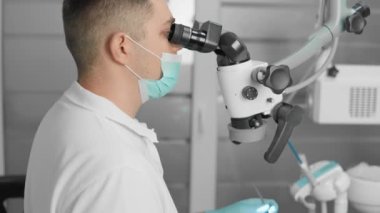 Bir dişçi, hastasının dişini tedavi etmek için mikroskop altında cerrahi işlem yapar. Diş sağlığı kliniğinin tıbbi personeli hastaya kapsamlı bakım sağlar. Profesyonel Tıp İşçisi