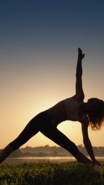 Gün doğumu ve yojik asanalarda yoga yaparken muhteşem manzaraya bakan kadın: güne ahenk ve pozitiflikle başlayın. Dikey video. Bir kadın vücudunu ve ruhunu geliştirmeye odaklanır.