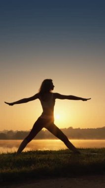 Bir kadın doğal bir huzur vahasında yojik asanalara odaklanır. Güneş ışığında yoga yaparak rahatlama ve uyum. Güneşin doğuşuyla ilgili çok güzel ve sportif bir kadının dikey videosu. Yüksek
